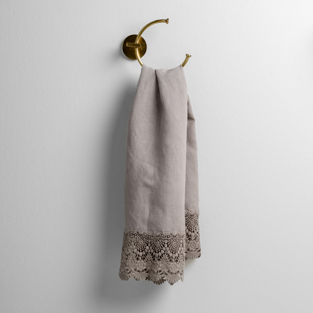 Fog: linen with mattine lace trimmed guest towel on a decorative towel ring mounted on a white wall. 