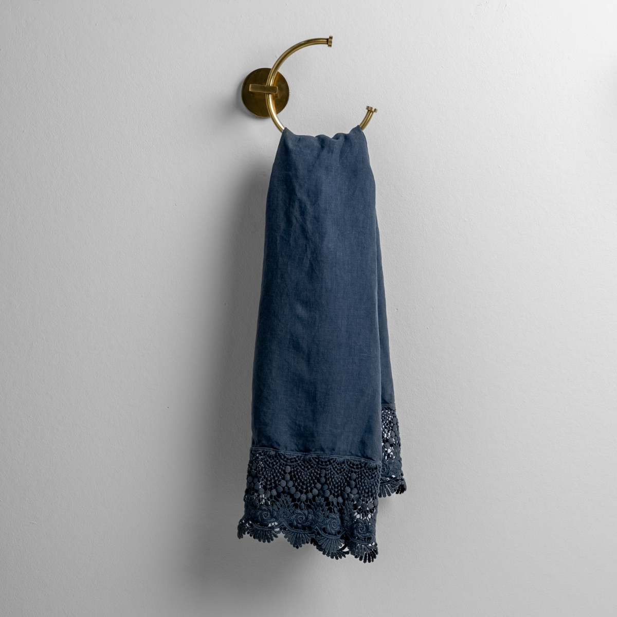 Midnight: linen with mattine lace trimmed guest towel on a decorative towel ring mounted on a white wall. 