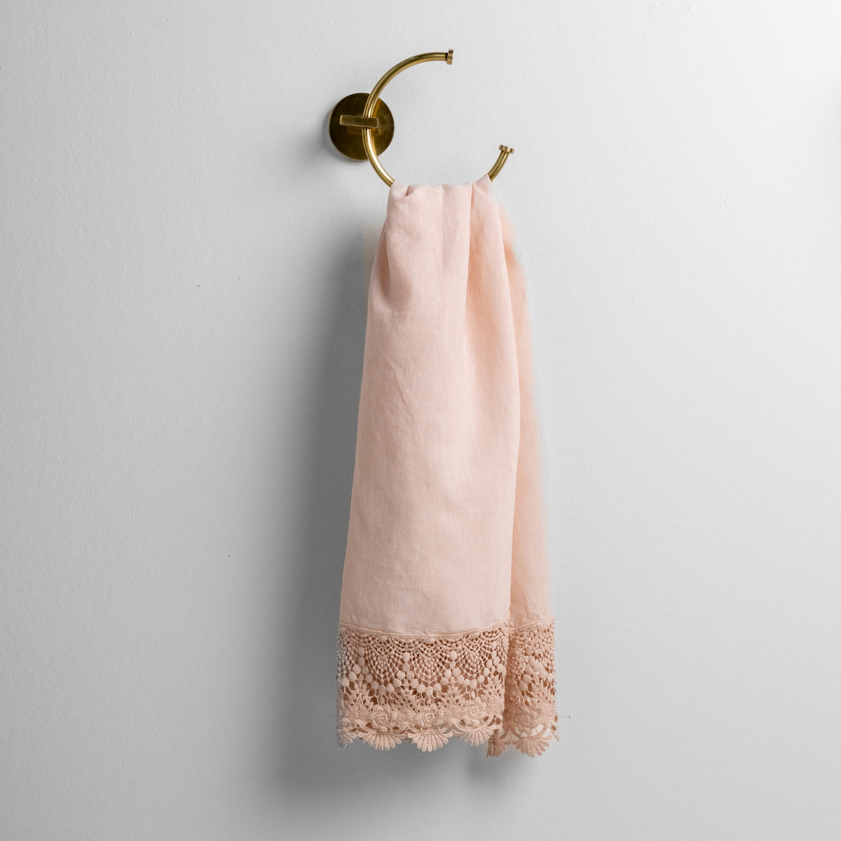 Pearl: linen with mattine lace trimmed guest towel on a decorative towel ring mounted on a white wall. 