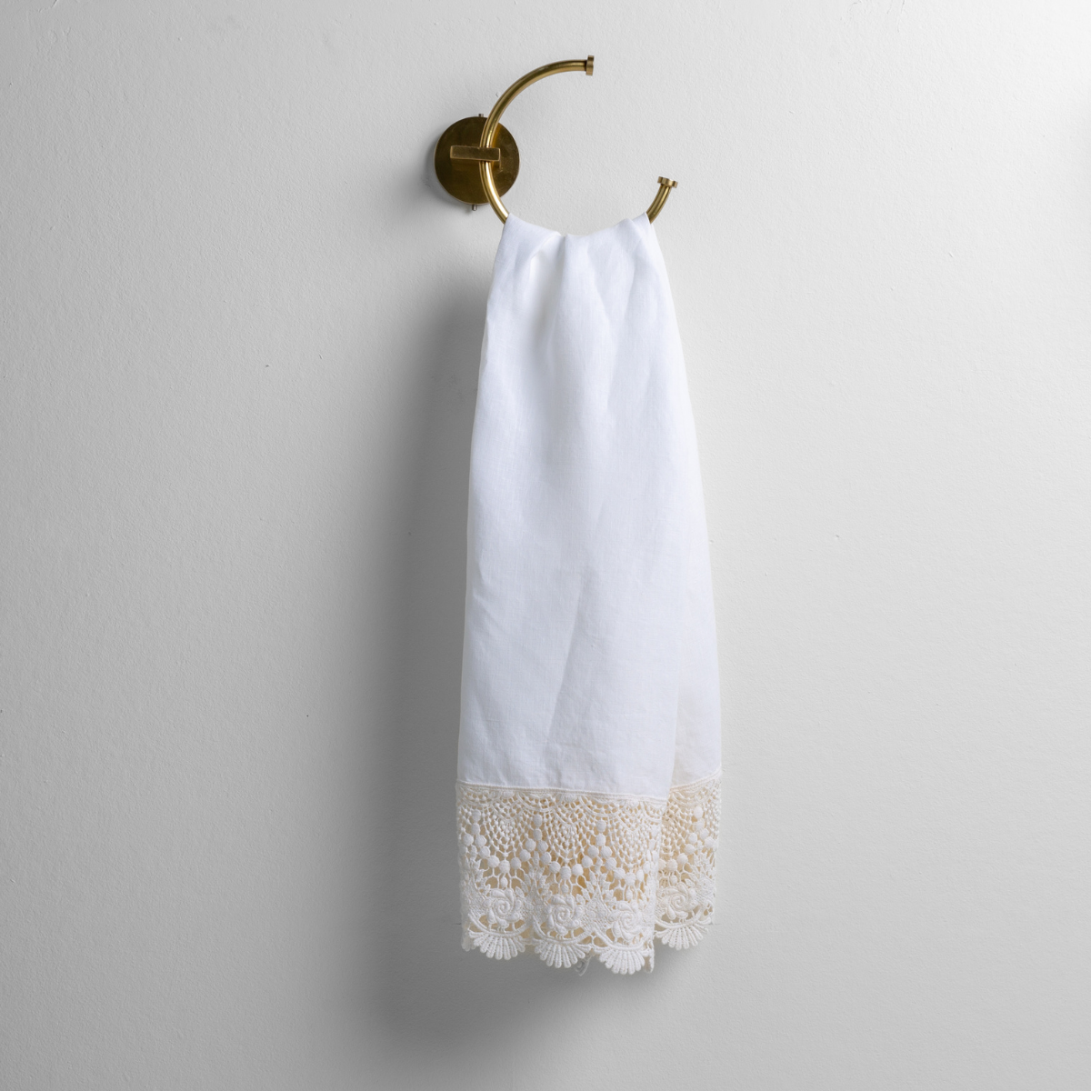 White: linen with mattine lace trimmed guest towel on a decorative towel ring mounted on a white wall. 