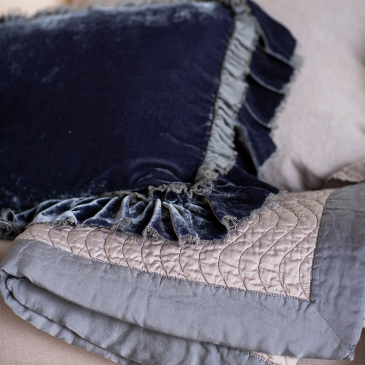French Lavender: a close up of a qulted cotton sateen blanket folded with a silk velvet throw pillow with raw edge ruffles.