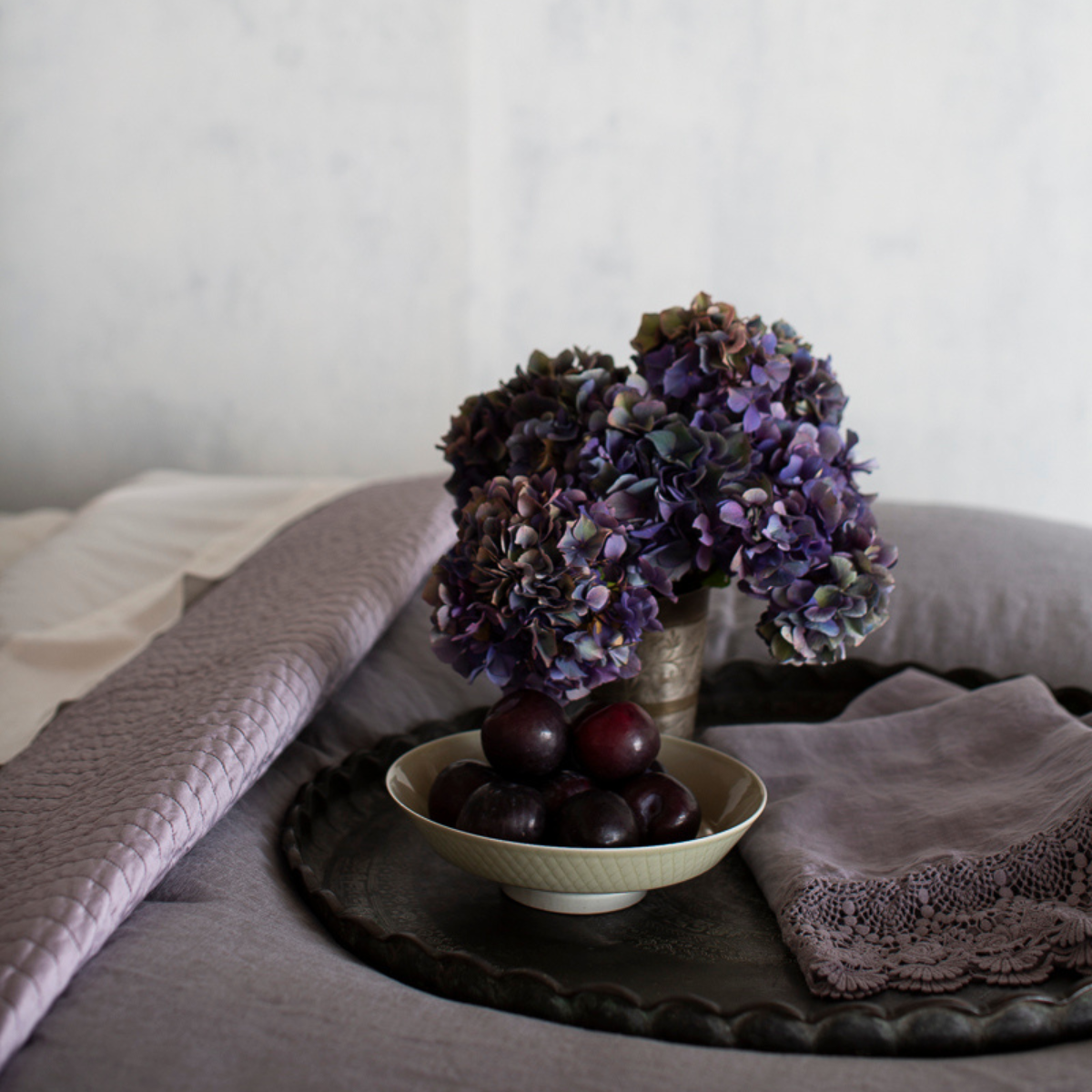 [allvariants]: a guest towel shown with a bowl of fruit and fresh flowers on a tray set on a monochromatic bed.