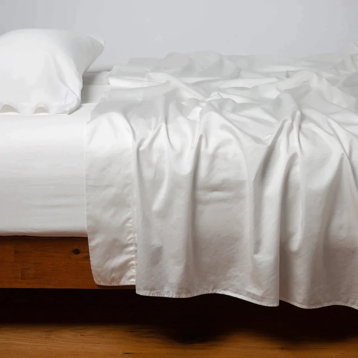 Winter White: Cotton sateen sleeping pillow, on a bed with matching sheets - side view.