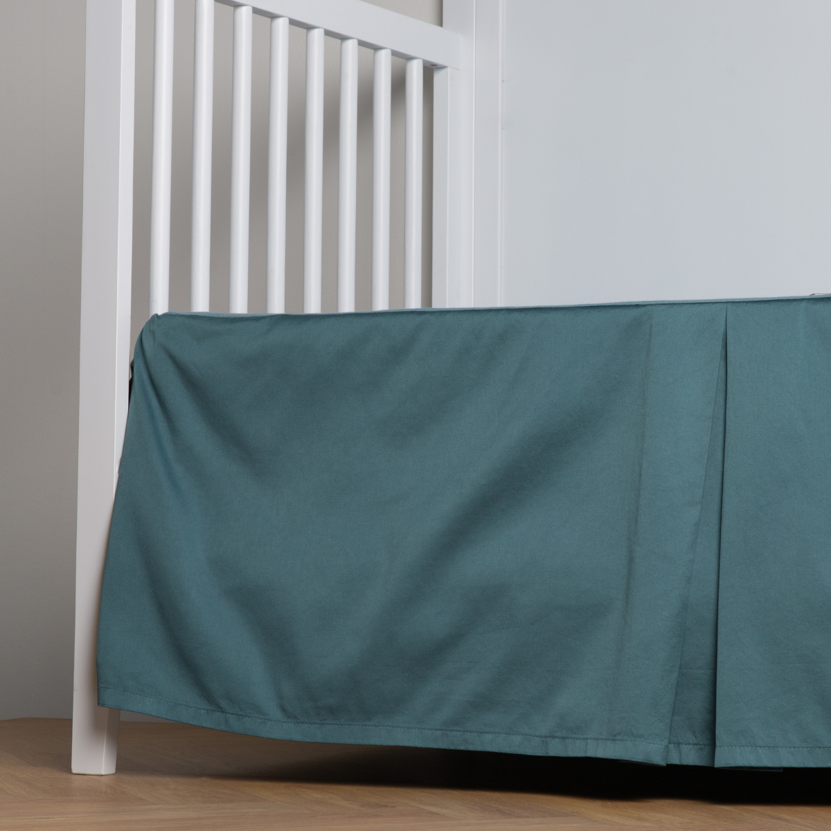 Cenote:  cotton sateen cribi skirt with a center pleat shown straight on from a slight angle in a crib without a crib mattress. 