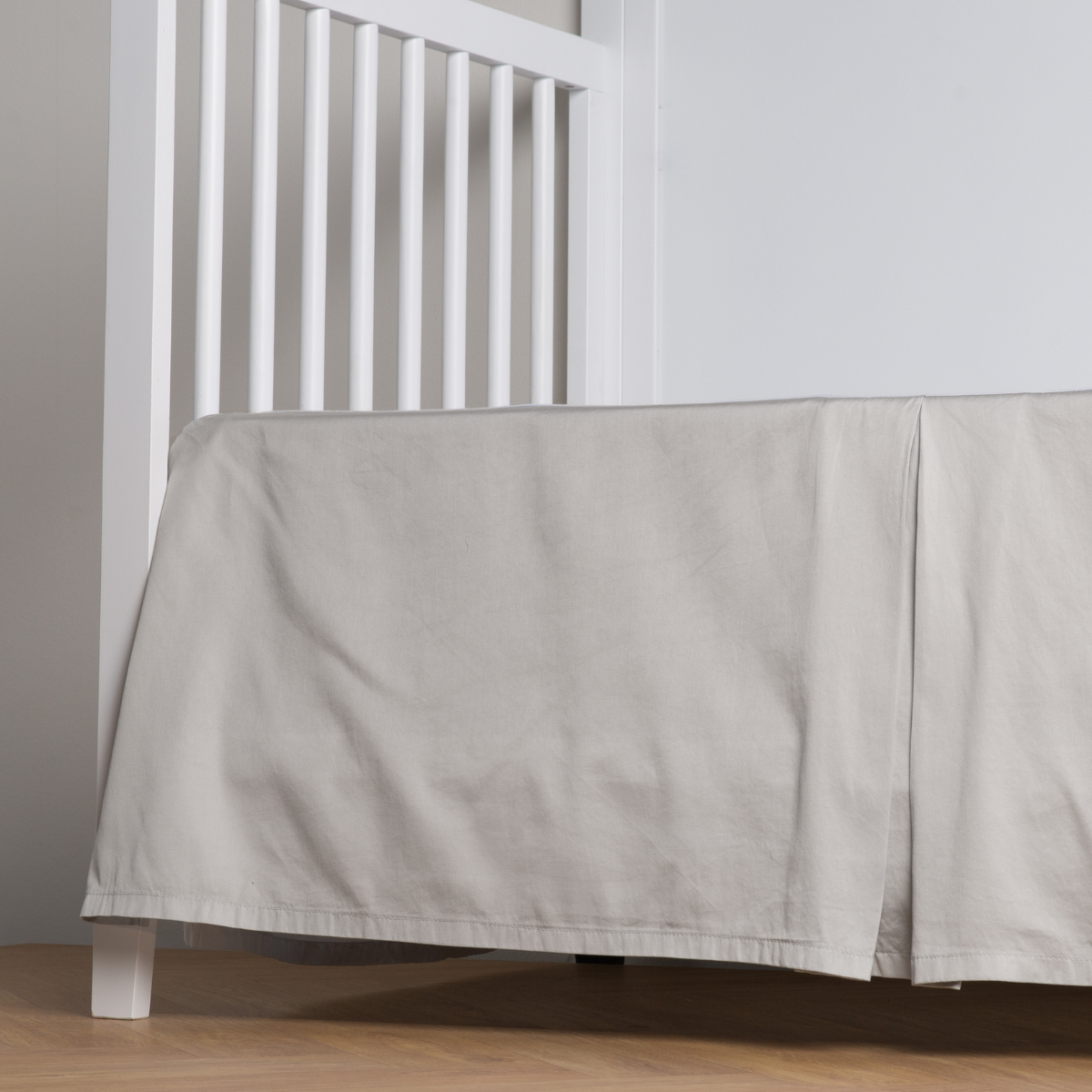 Cloud:  cotton sateen cribi skirt with a center pleat shown straight on from a slight angle in a crib without a crib mattress. 