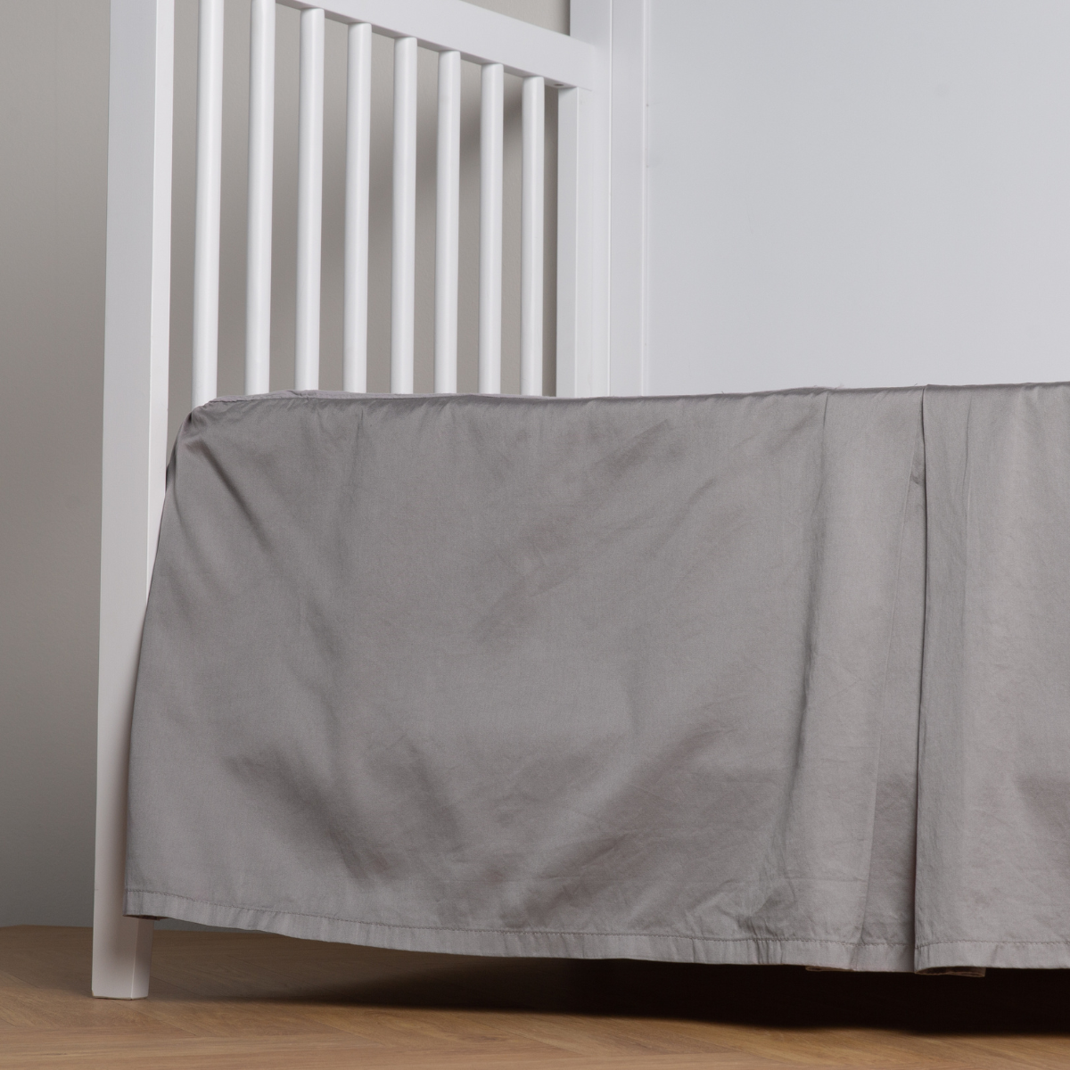 Moonlight:  cotton sateen cribi skirt with a center pleat shown straight on from a slight angle in a crib without a crib mattress. 