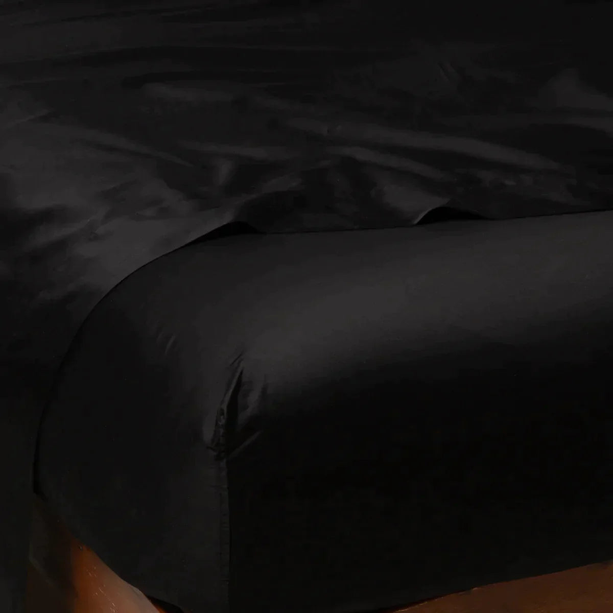 Corvino: Cotton sateen flat sheet draped over matching fitted sheet. Shown from the top corner, the flat sheet is rumpled, highlighting the shine of the fabric.