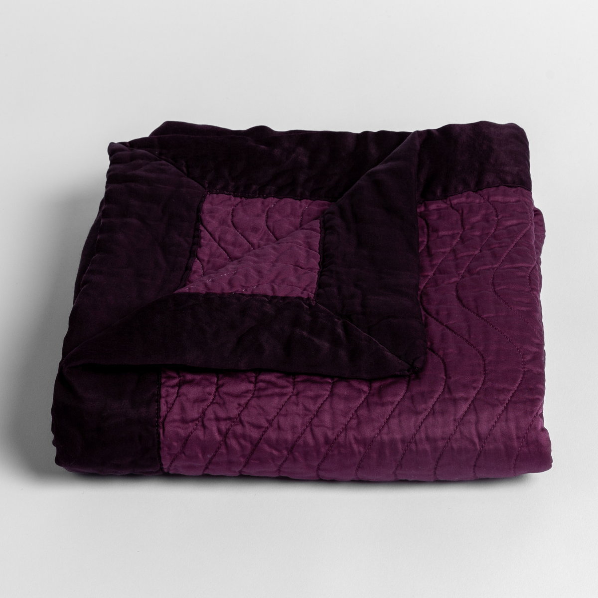 Fig: a folded quilted cotton sateen baby blanket with its corner folded down to show the trim contrast - shot against a white background. 