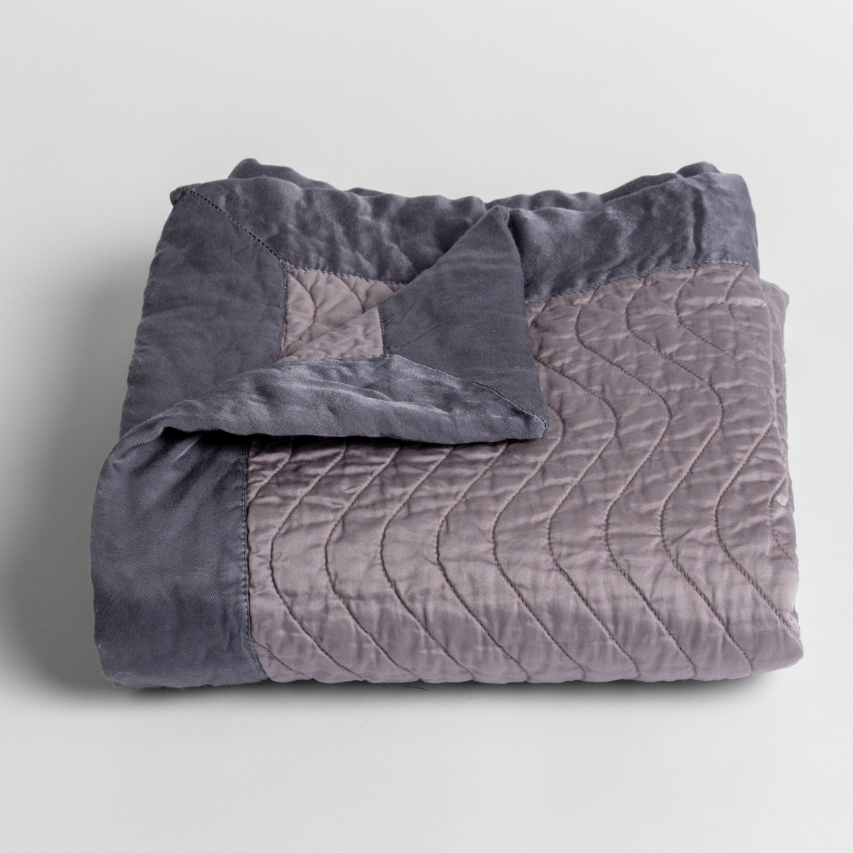 French Lavender: a folded quilted cotton sateen baby blanket with its corner folded down to show the trim contrast - shot against a white background. 