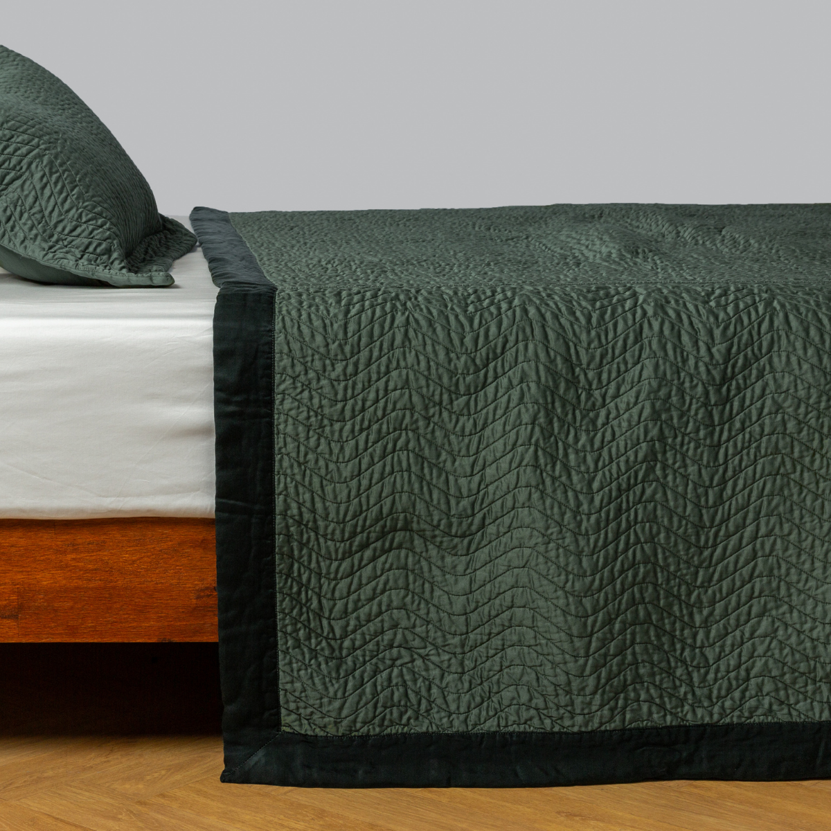 Juniper: quilted cotton sateen coverlet with matching sham on a winter white fitted sheet - side view. 