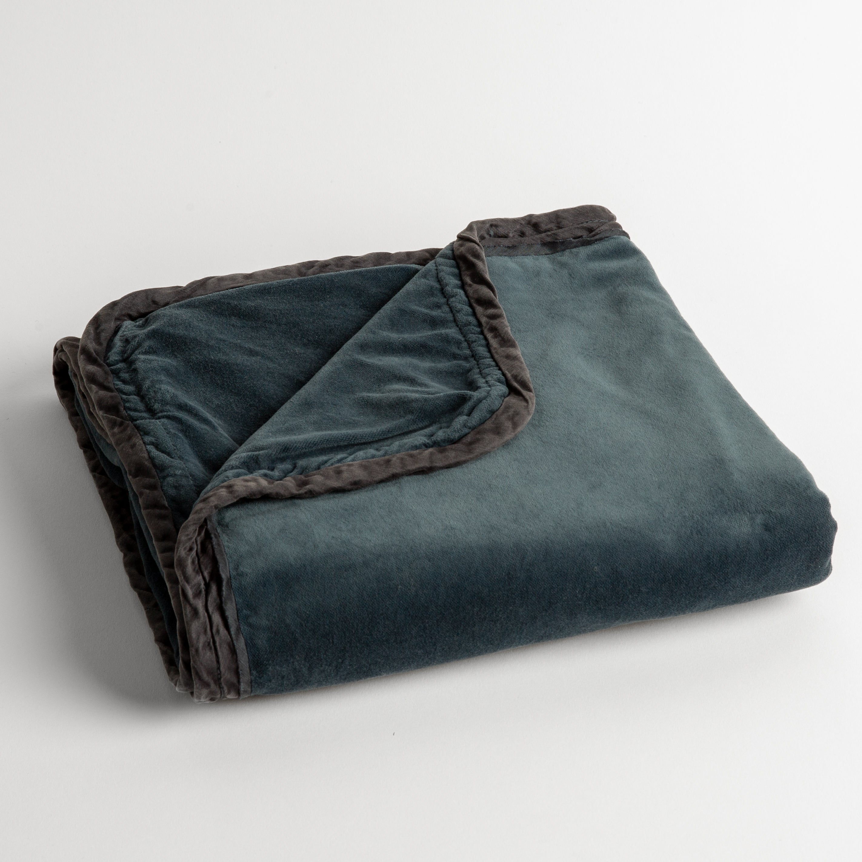 Midnight: cotton velvet baby blanket trimmed with charmeuse, folded with a covern folded back to show trim contrast; shot overhead and at a slight angle against a white background. 