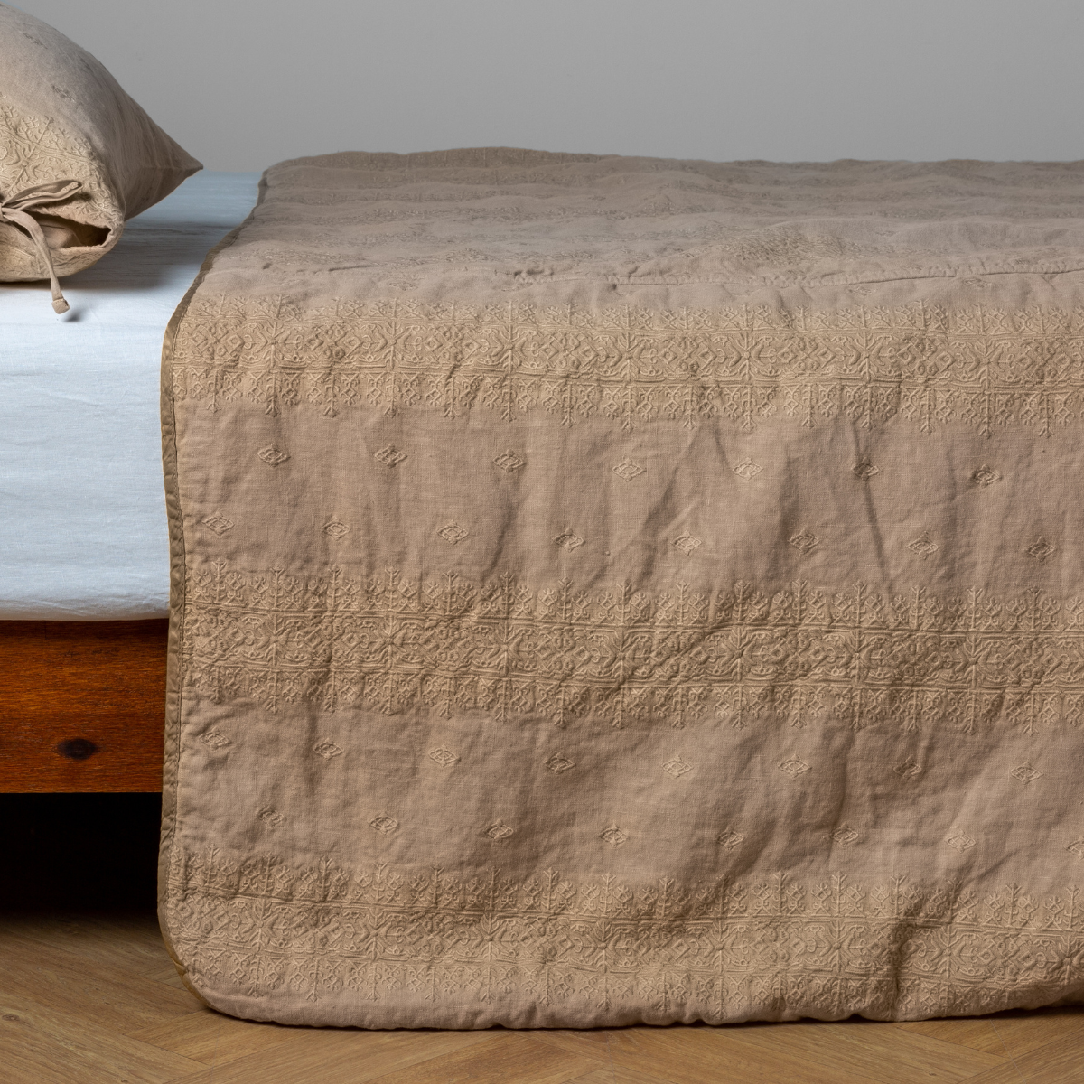 Honeycomb:  embroidered midweight linen bedspread with matching sham on a bed with a white fitted sheet. Shot from the side view, the bedframe is slightly visible  against a white background and medium wood floor. 