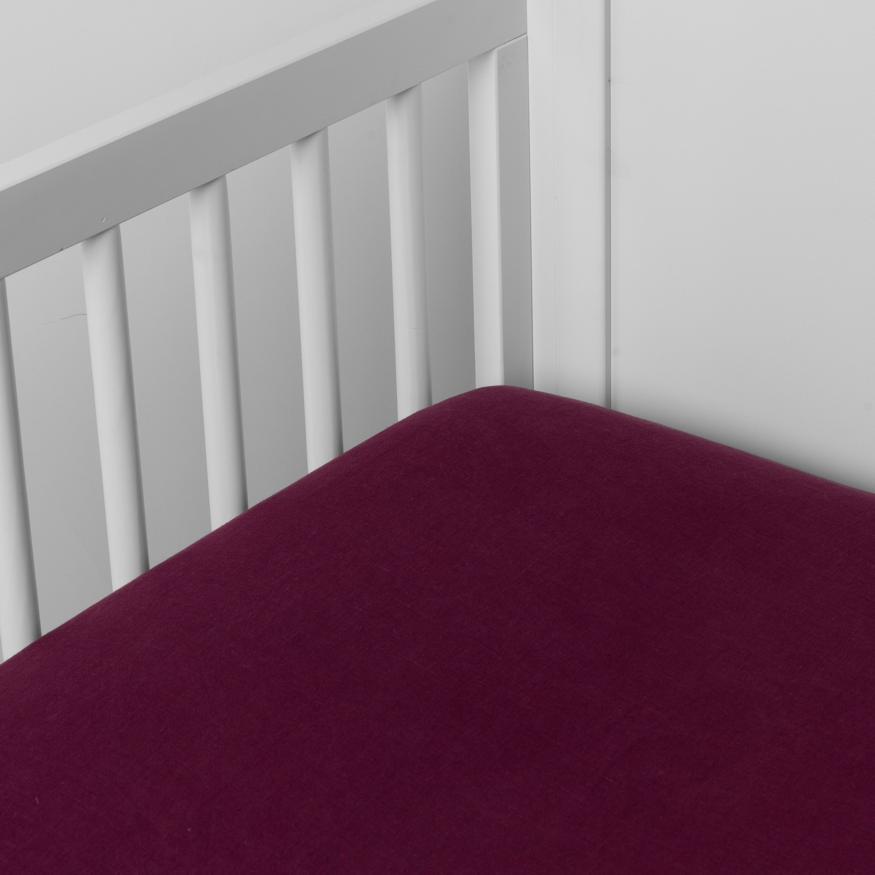 Fig: linen crib sheet on the mattress shot slightly overhead into the corner of a white crib. against a white background. 
