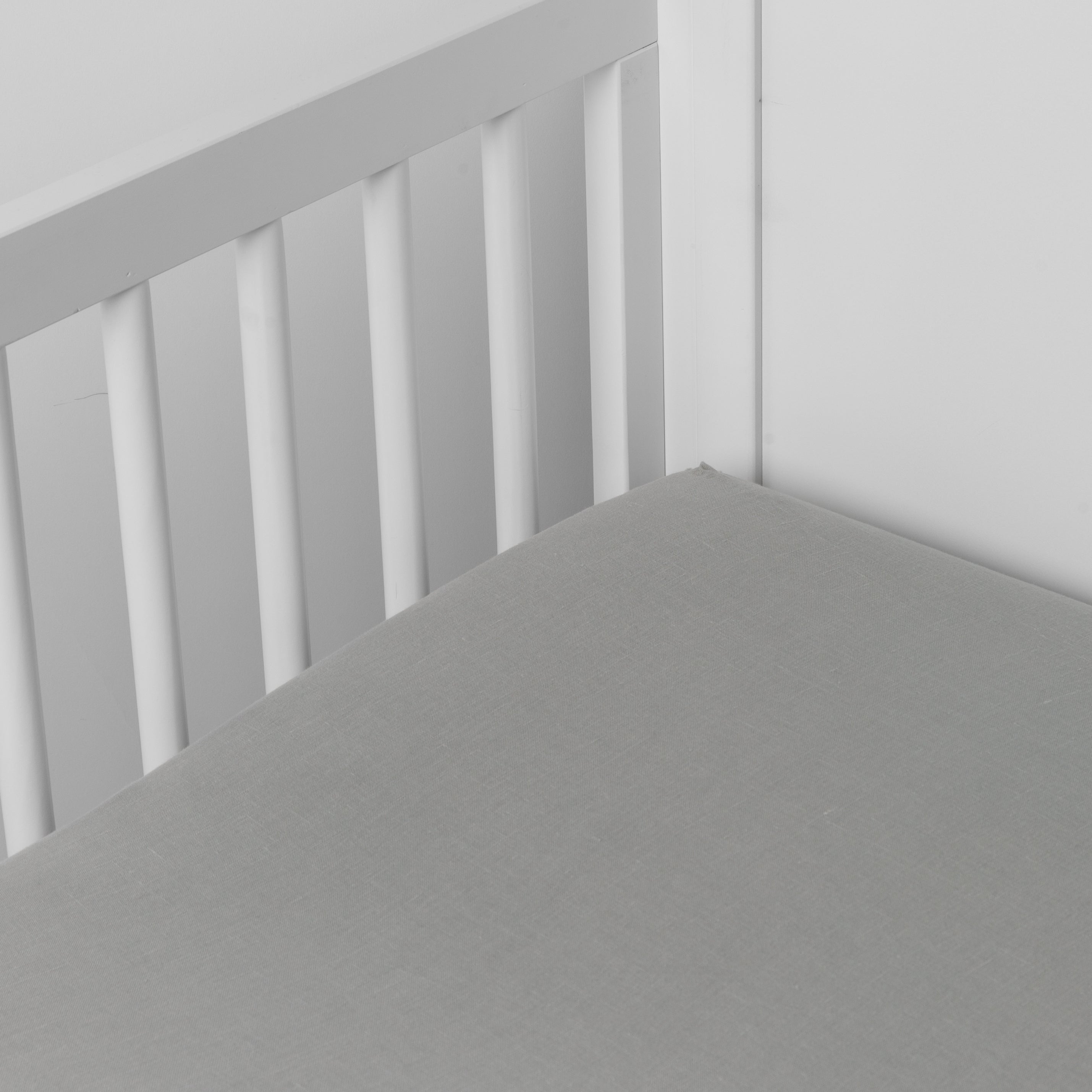 Mineral: linen crib sheet on the mattress shot slightly overhead into the corner of a white crib. against a white background. 