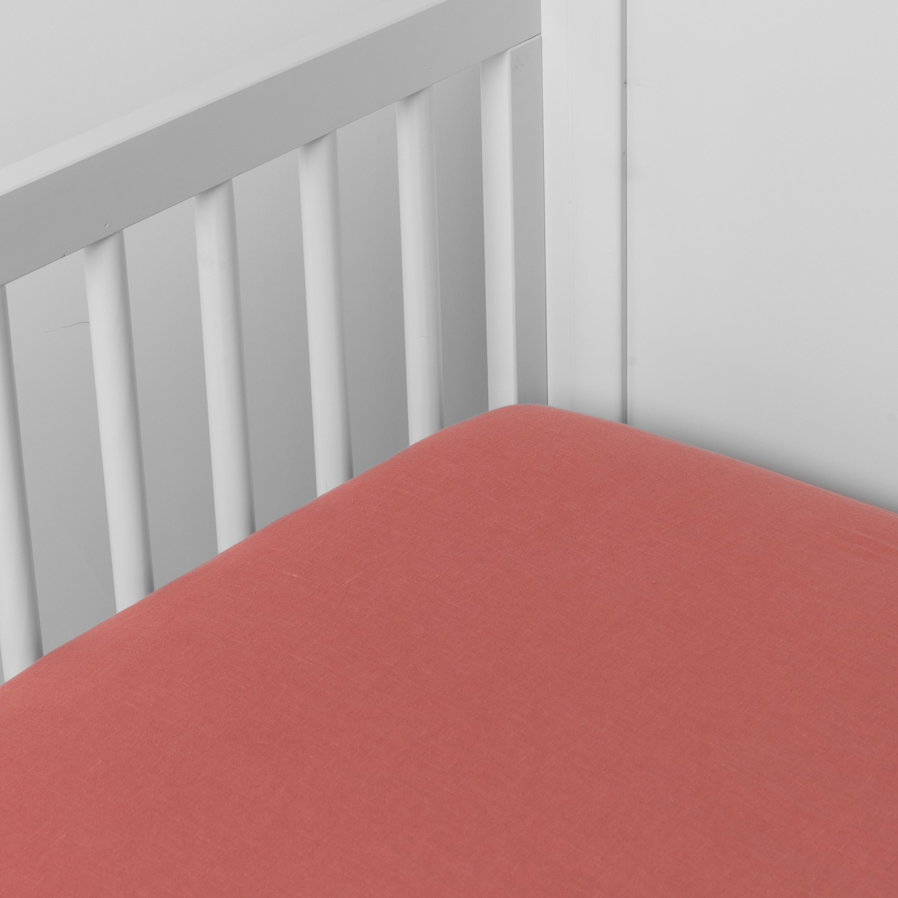 Poppy: linen crib sheet on the mattress shot slightly overhead into the corner of a white crib. against a white background. 