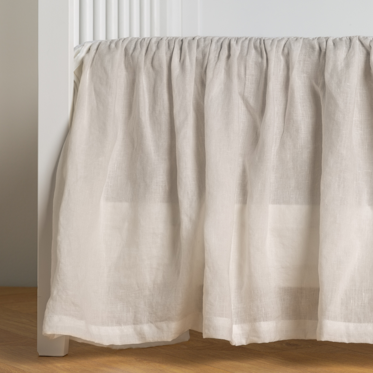 Winter White:   crib skirt shown on a white crib with no mattress against a white wall and medium wood flooring. 