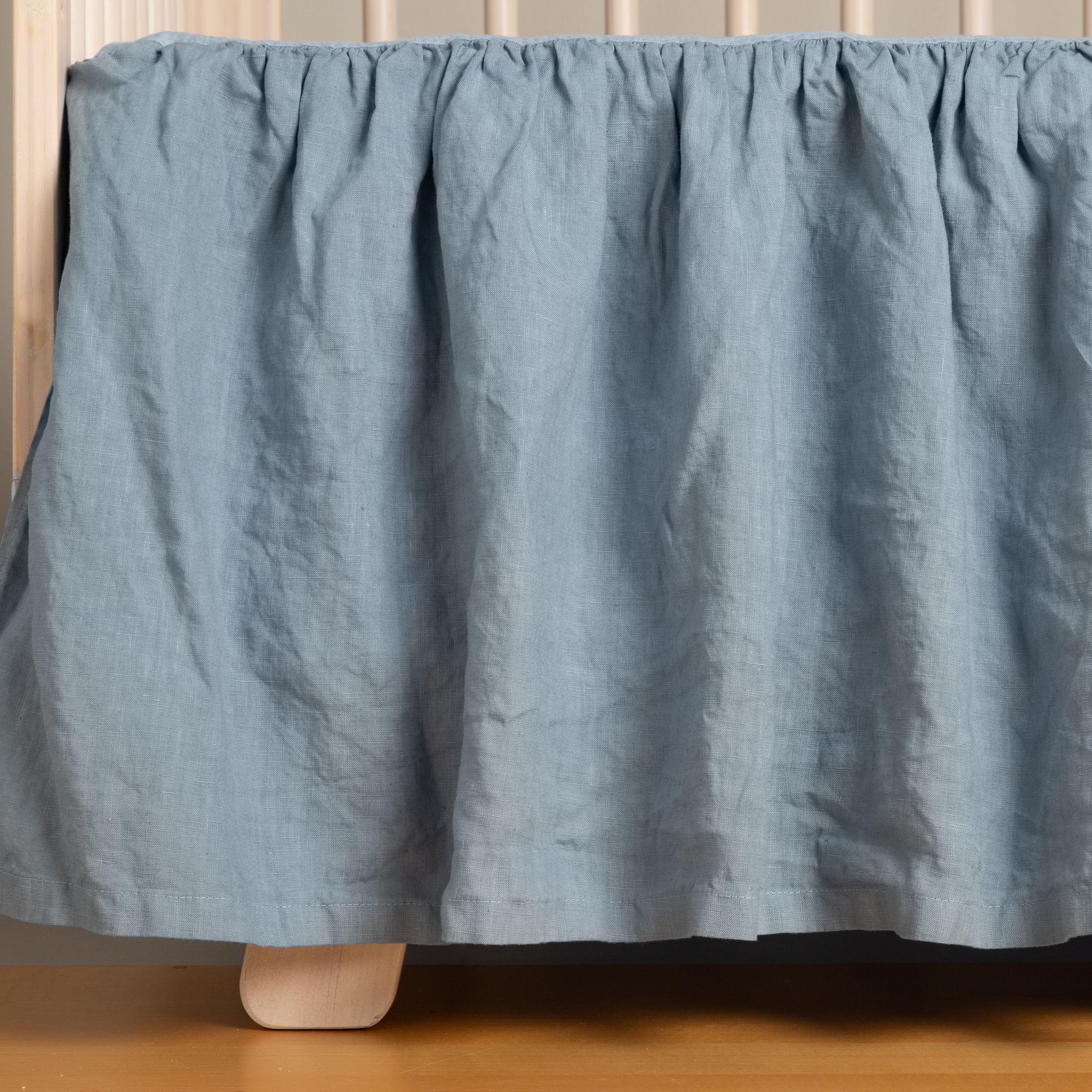 Tahoe Blue: a crib skirt on a natural wood crib on a medium wood floor. 