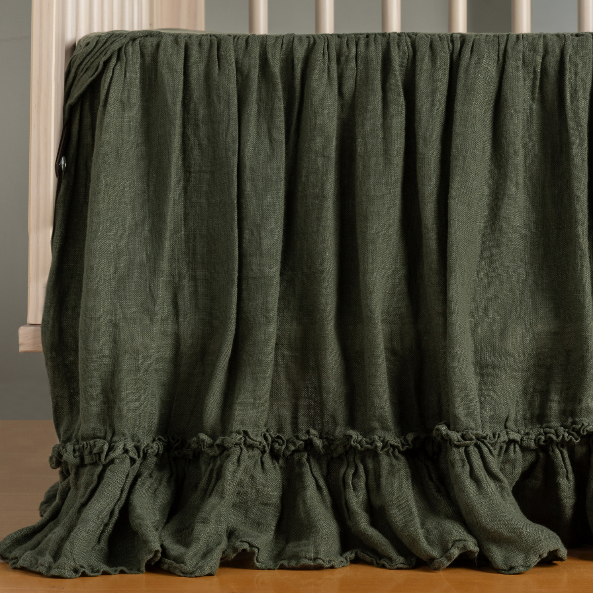 Juniper: ruffled crib skirt shown on a crib with no crib mattress - the ruffle gently pooling on the floor. 