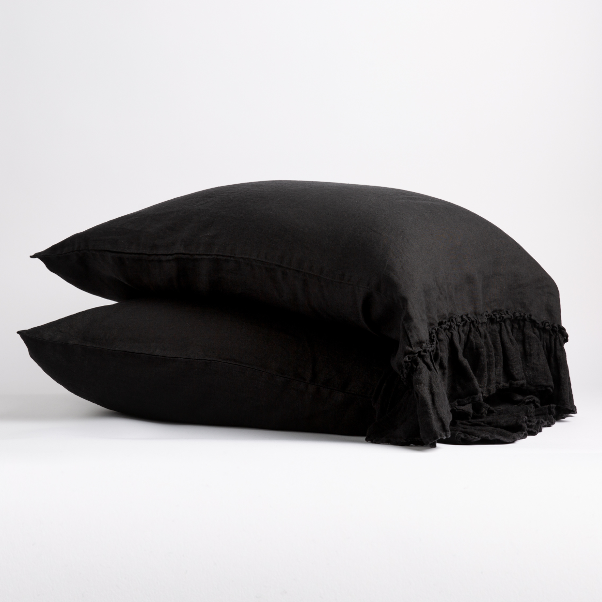 Corvino: Two sleeping pillows stacked at a slight angle against a plain background, showcasing ruffle trim detail - side view.