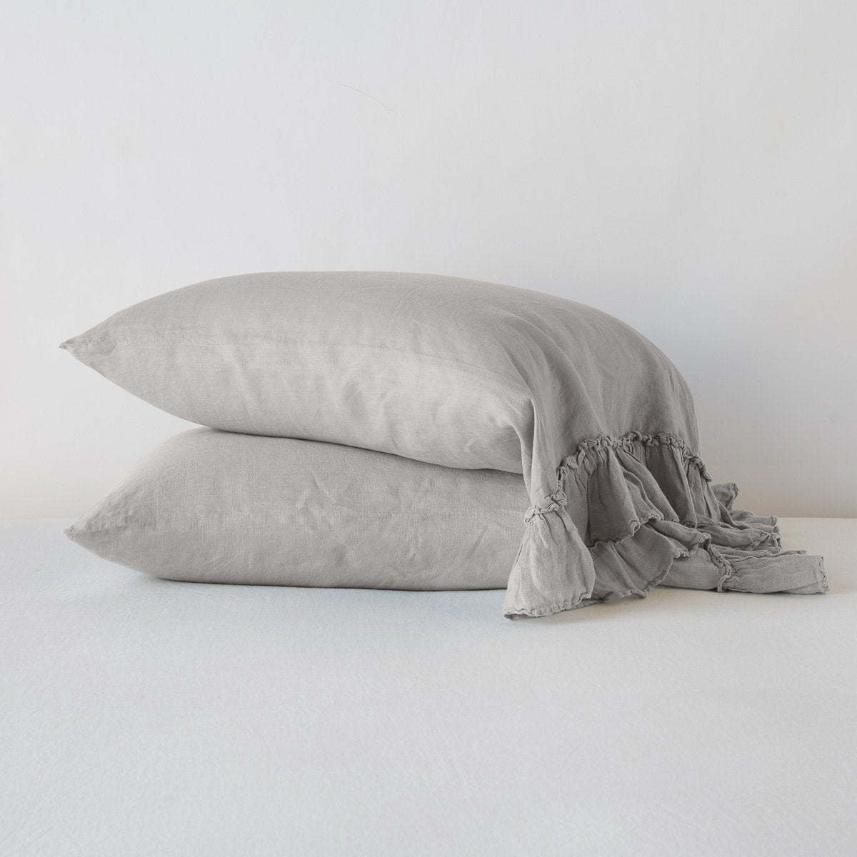 [allvariants]: Two Linen Whisper sleeping pillows, stacked at a slight angle against a plain background, showcasing ruffle trim detail - fog, side view.