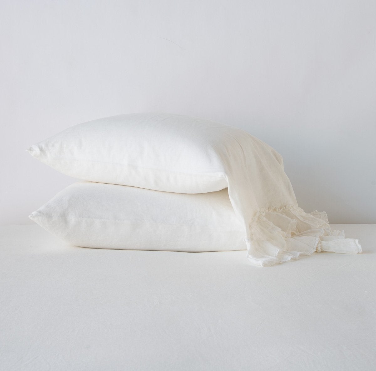 Winter White: Two sleeping pillows stacked at a slight angle against a plain background, showcasing ruffle trim detail - side view.