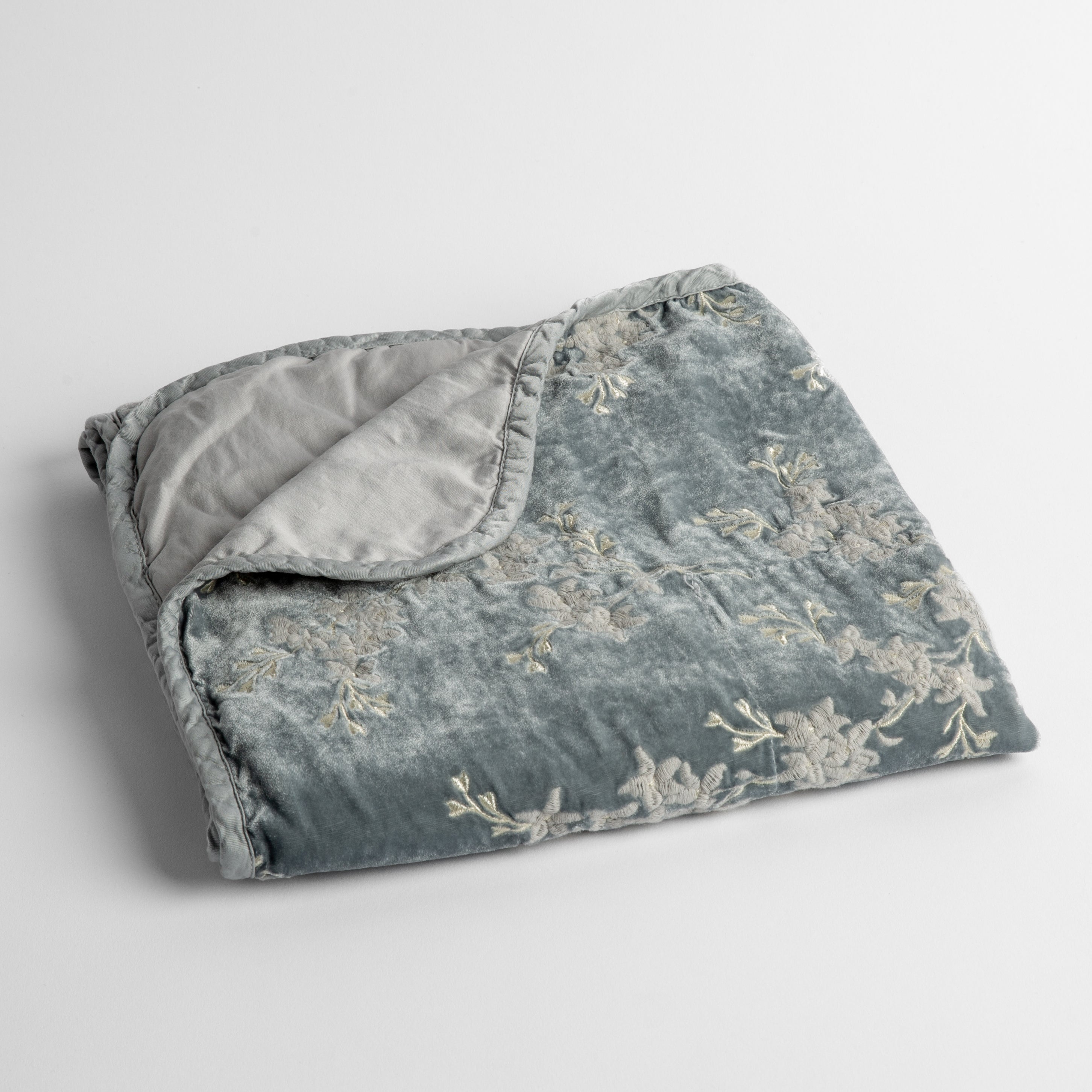 Cloud: embroidered silk velvet baby blanket folded with a corner folded back to show the trim and back of the blanket - shot overhead at a slight angle against a white background. 