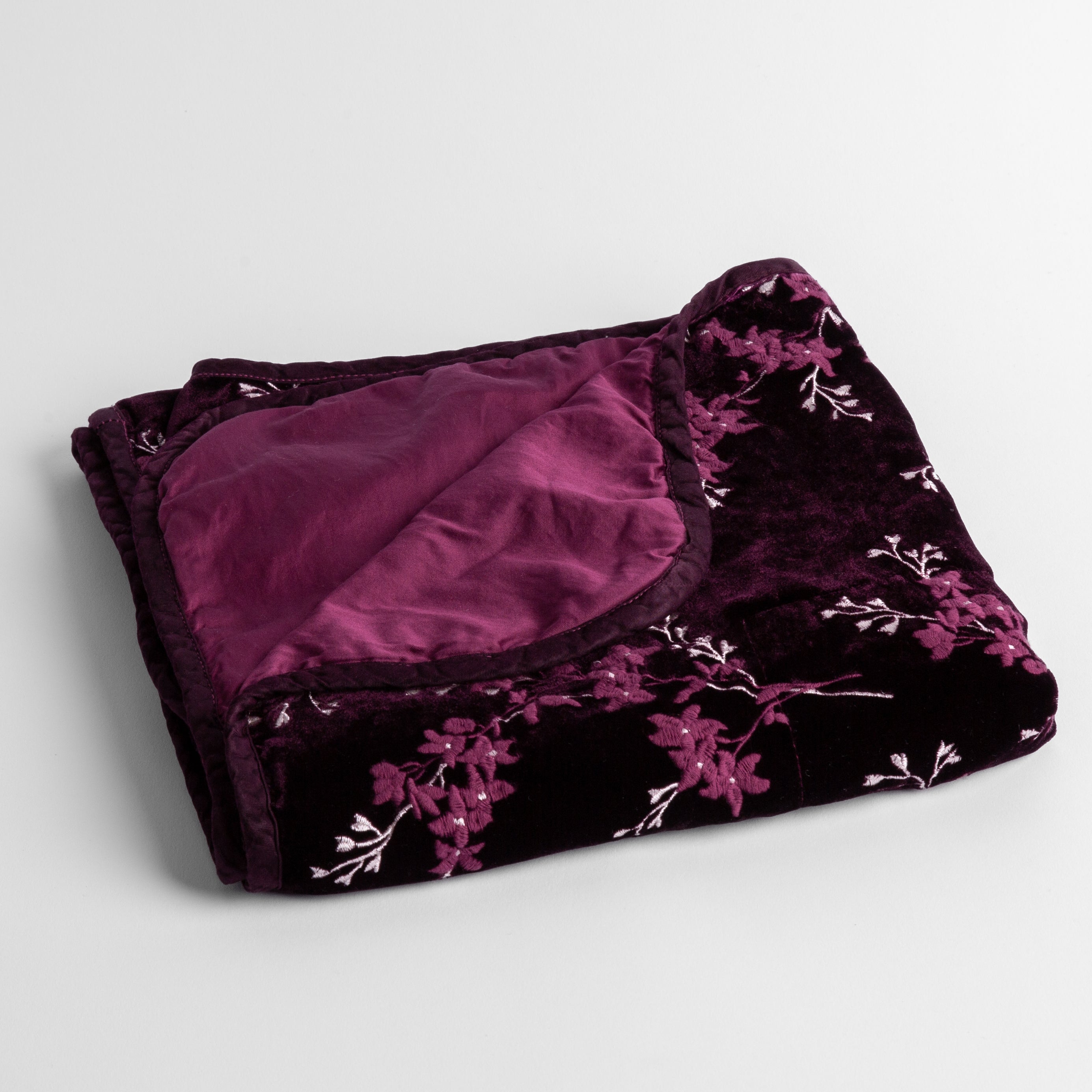 Fig: embroidered silk velvet baby blanket folded with a corner folded back to show the trim and back of the blanket - shot overhead at a slight angle against a white background. 