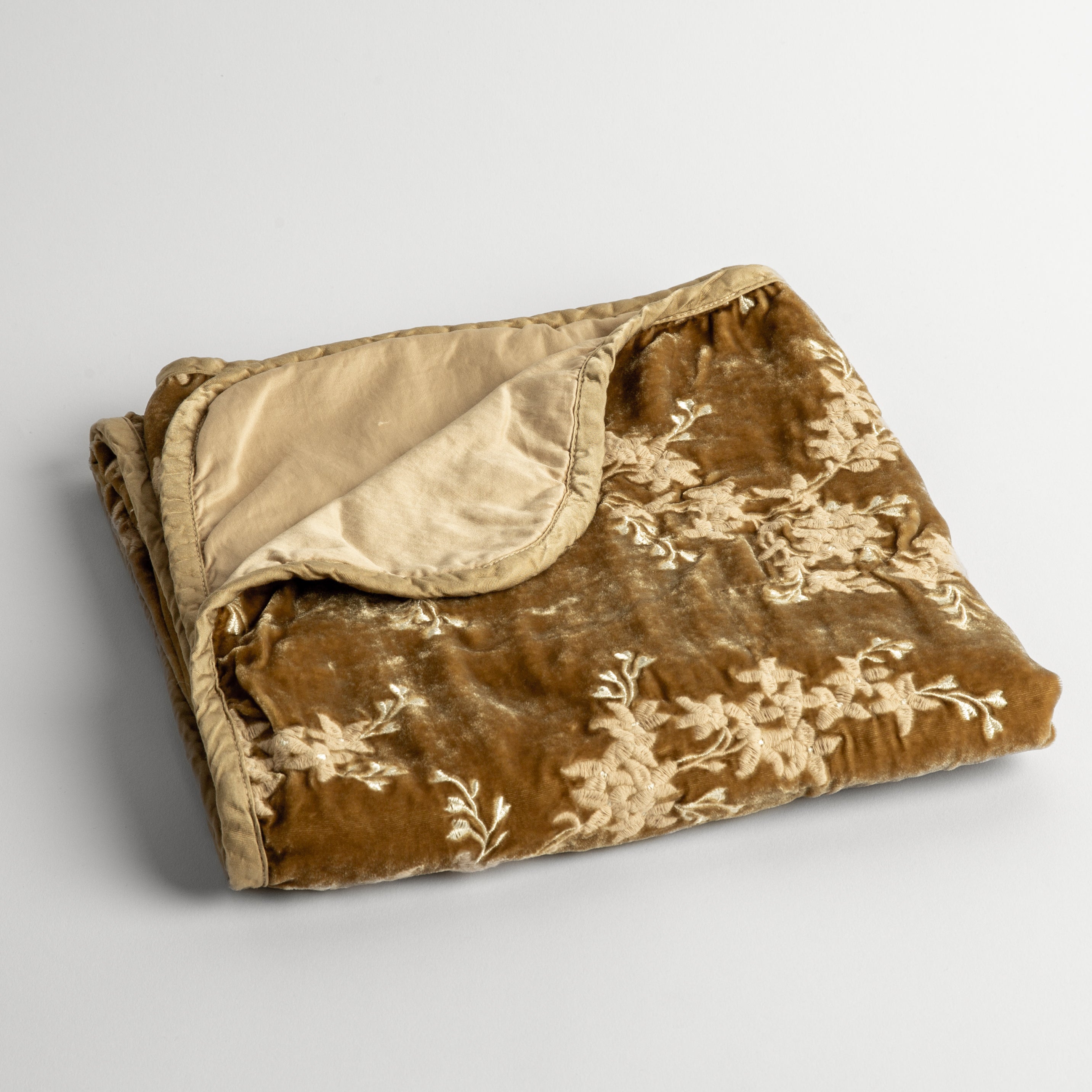 Honeycomb: embroidered silk velvet baby blanket folded with a corner folded back to show the trim and back of the blanket - shot overhead at a slight angle against a white background. 