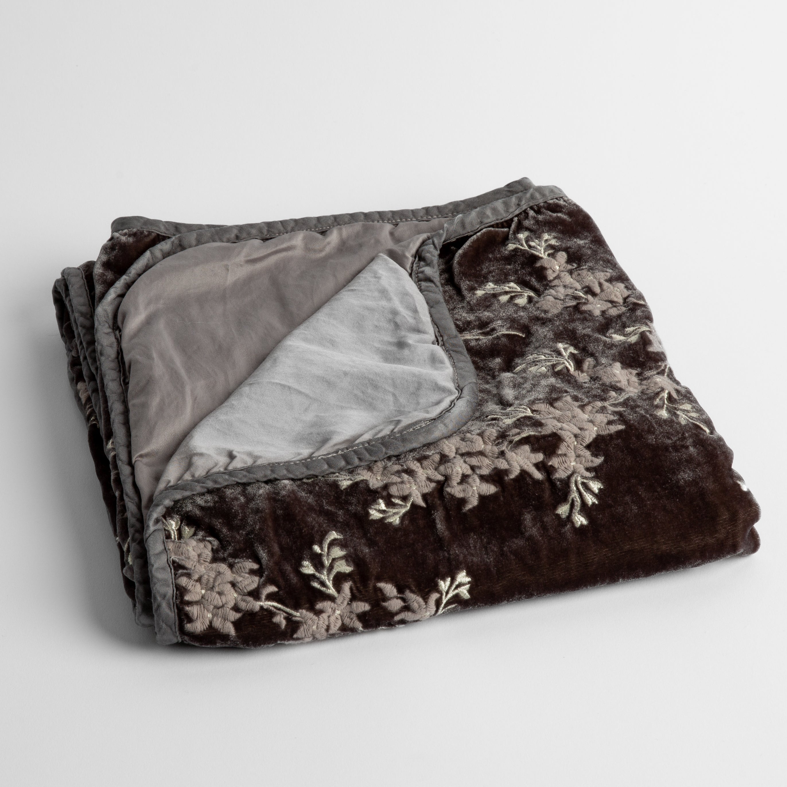 Moonlight: embroidered silk velvet baby blanket folded with a corner folded back to show the trim and back of the blanket - shot overhead at a slight angle against a white background. 