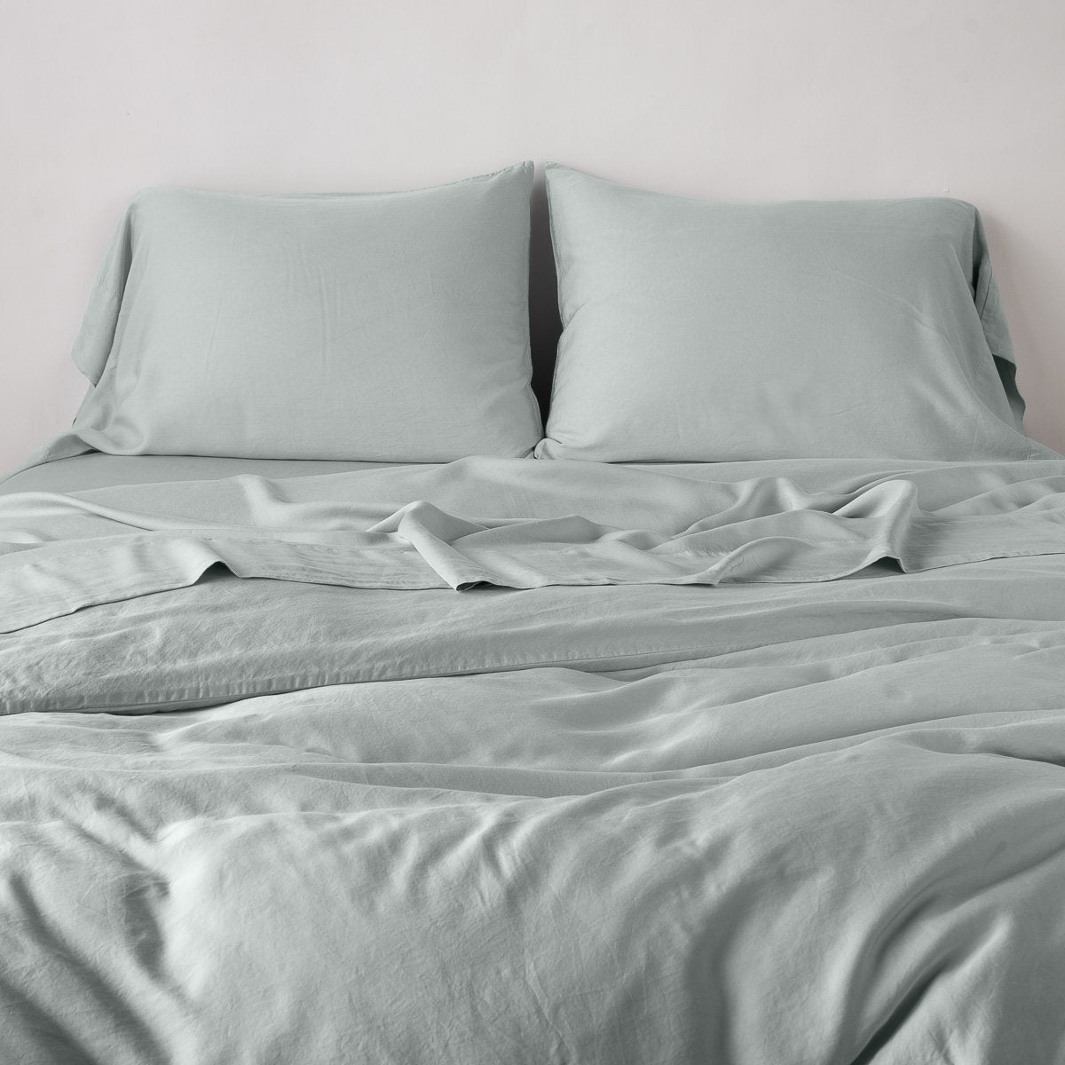 Eucalyptus: duvet cover with matching sleeping pillows and sheeting against a white wall - end of bed view.