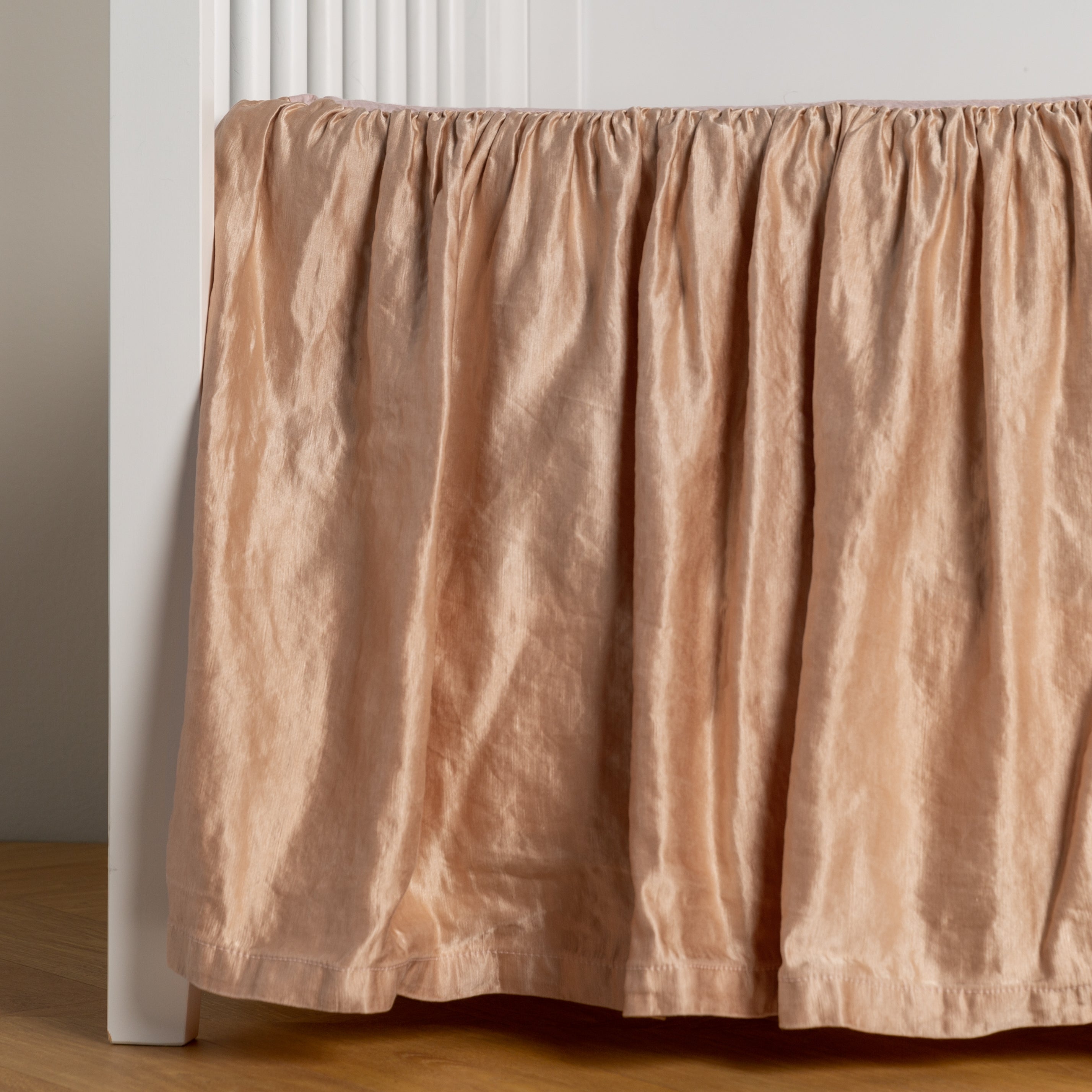 Rouge: charmeuse crib skirt shown on a white crib against a white wall and medium wood floor. 