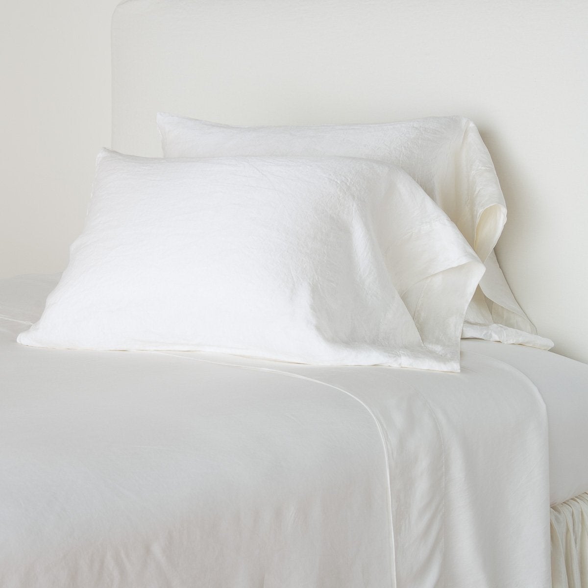 : Paloma sleeping pillows leaning upright against a white wall on monochromatic sheeting - winter white, cropped three-quarter angle.