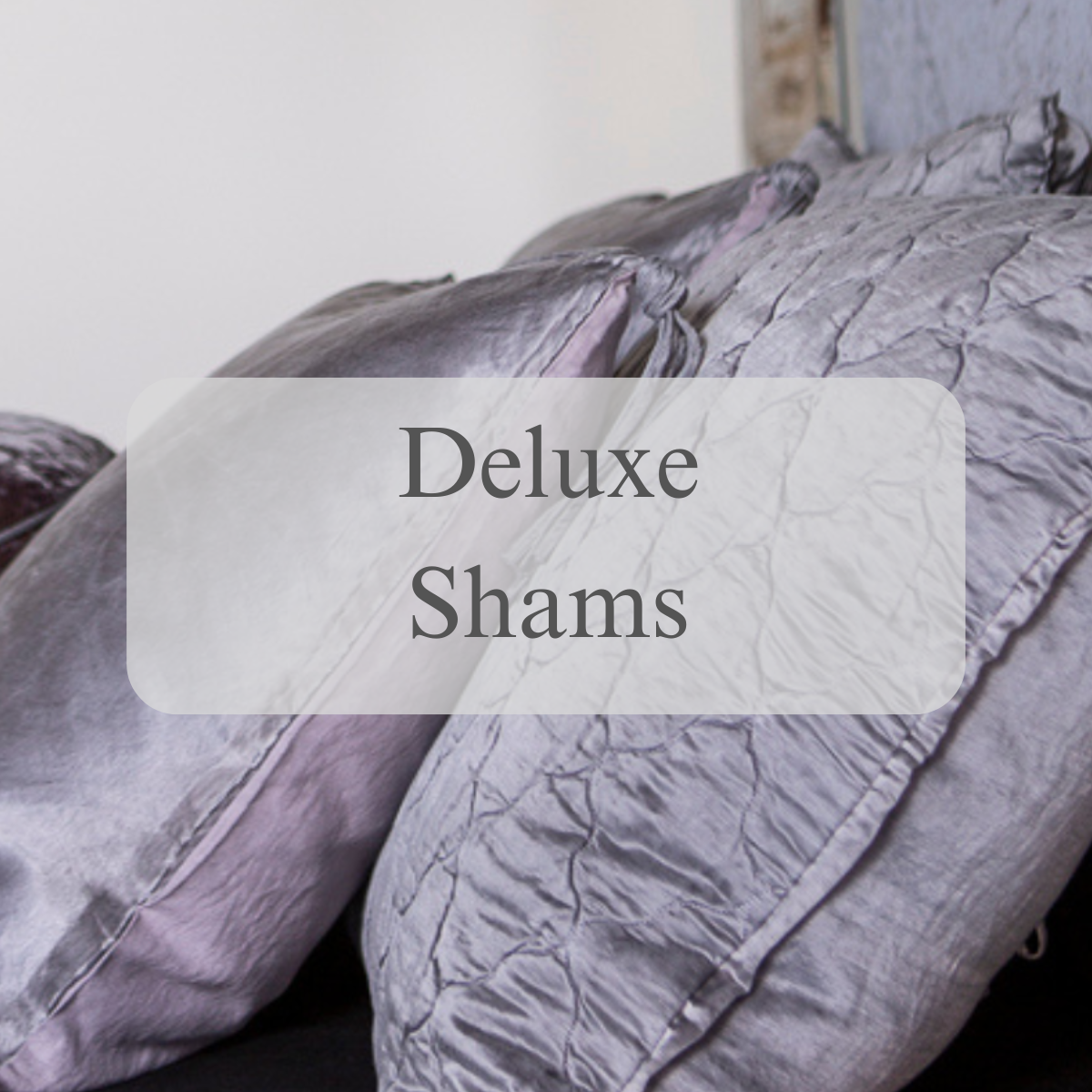 A shot of shams and pillows in lavender tones with a text overlay that reads Deluxe Shams