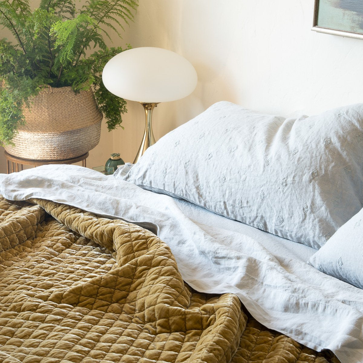 : Silk velvet coverlet in rich honeycomb, rumpled under linen sheets and silk charmeuse sleeping pillows in soft blue green - cropped three-quarter angle.