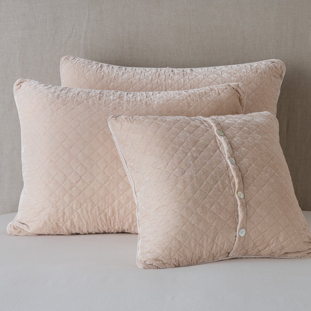 [allvariants]: Silk velvet quilted shams leaning upright against a neutral headboard. One sham is backwards to showcase the shimmering shell button closure - pearl.