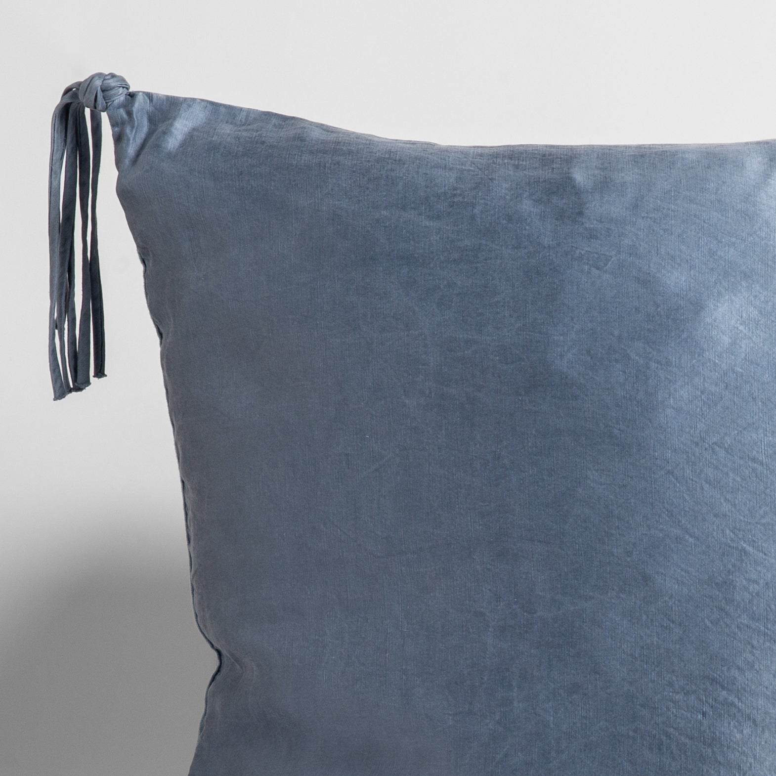 Tahoe Blue: close up of a charmeuse pillow corner and tassel against a white background. 