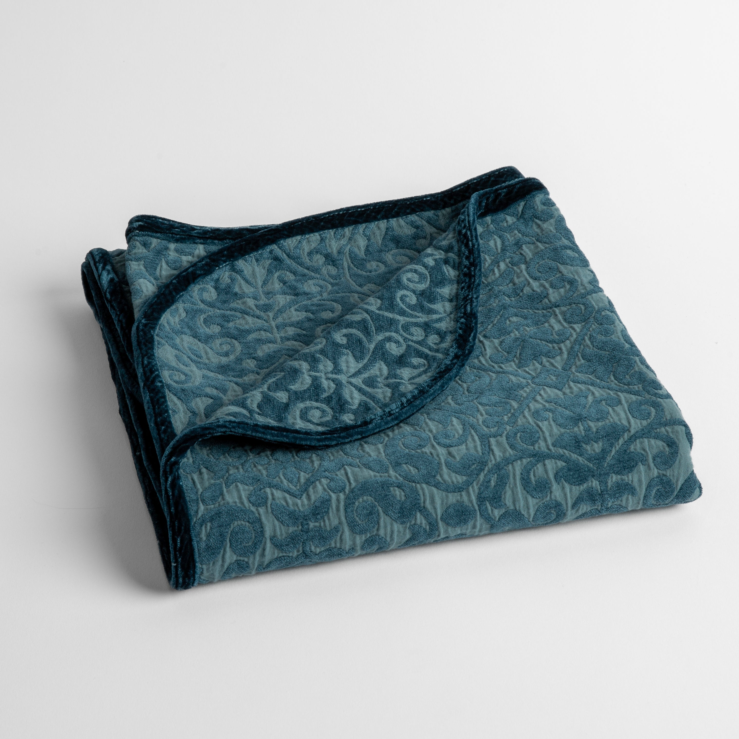Cenote: a folded cotton chenille baby blanket trimmed in silk velvet shot overhead at a slight angle against a white background. 