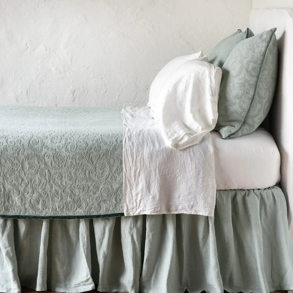 Eucalyptus: The Adele coverlet in eucalyptus, on a bed viewed from the side against a plain white wall. The bed is styled neatly with the coverlet folded back to reveal white sheets, bed skirt and pillows.