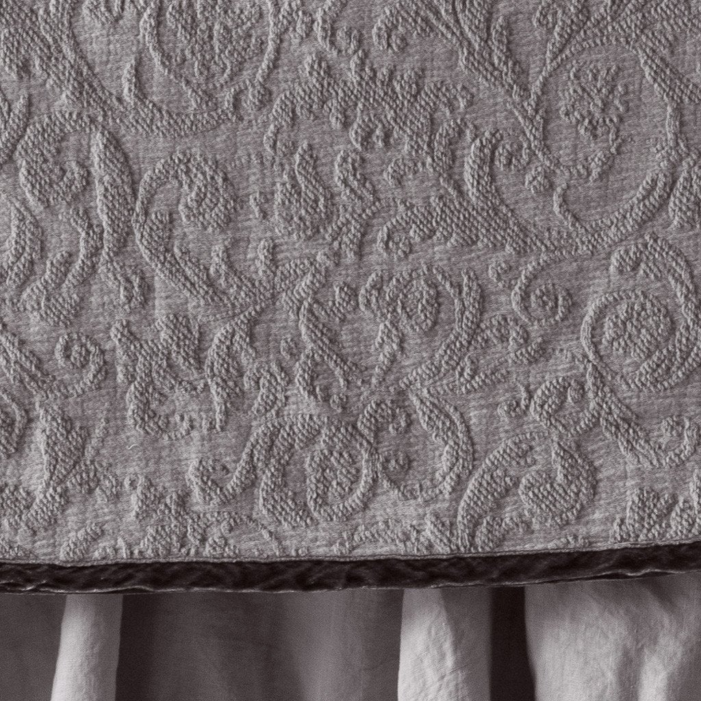 Fog: Close up of the Adele coverlet in fog, highlighting the detail of the cotton damask and the silk velvet edging trim. A white bed skirt peeks out at the bottom of the shot.