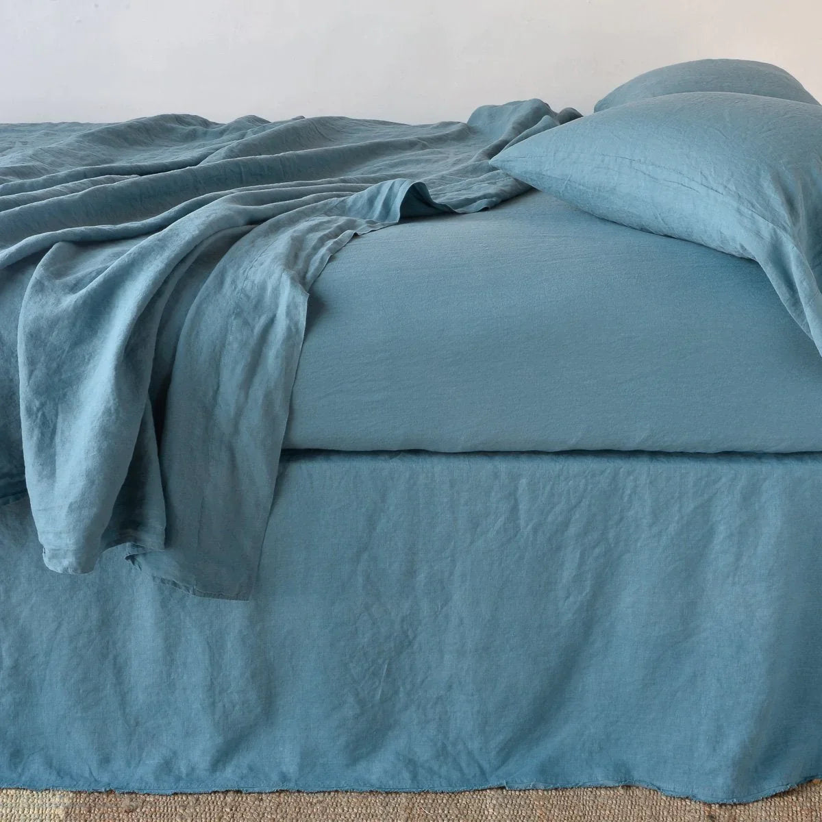 Cenote: Austin bed skirt in cenote shown from the side on a bed with monochromatic sheeting, highlighting its tailored, ungathered style.