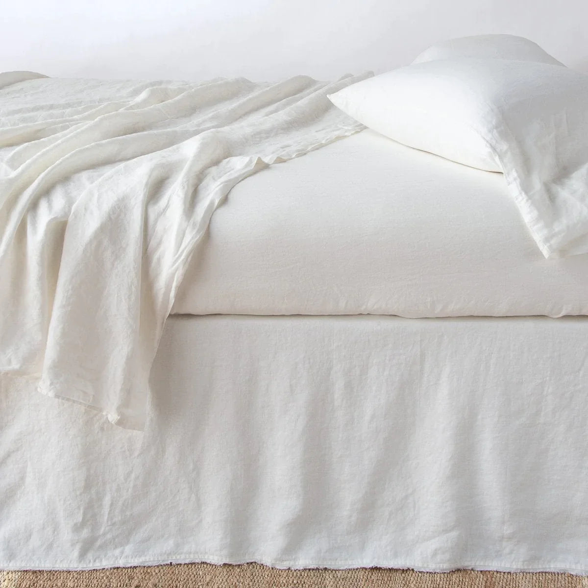 Winter White: Austin bed skirt in winter white shown from the side on a bed with monochromatic sheeting, highlighting its tailored, ungathered style.