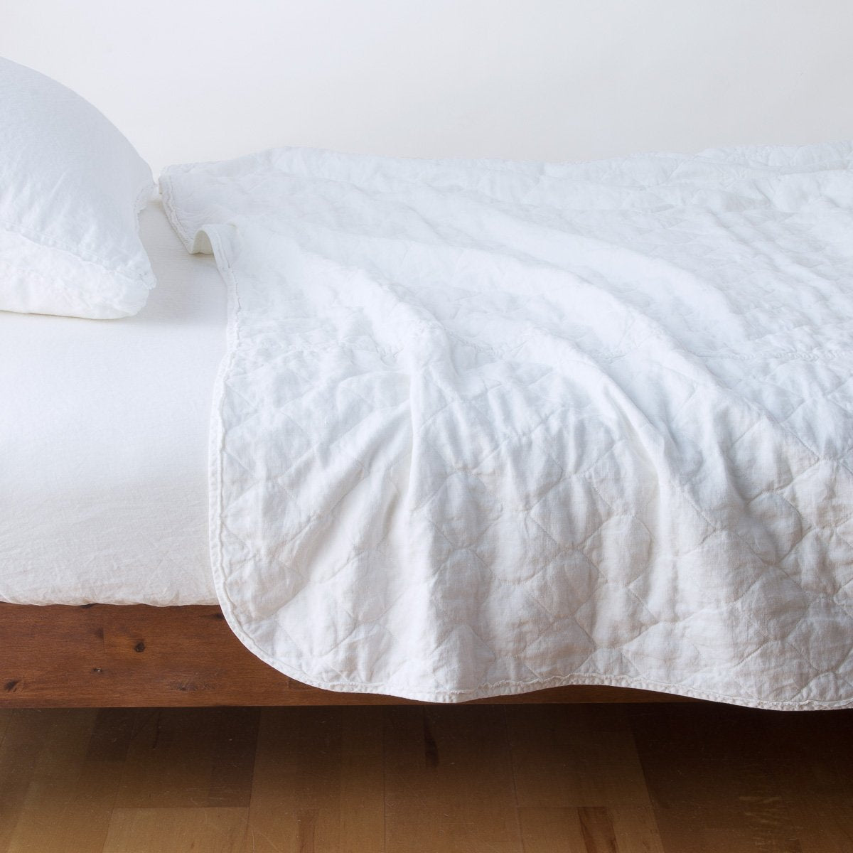 White: quilted midweight linen coverlet on a bed - side view.