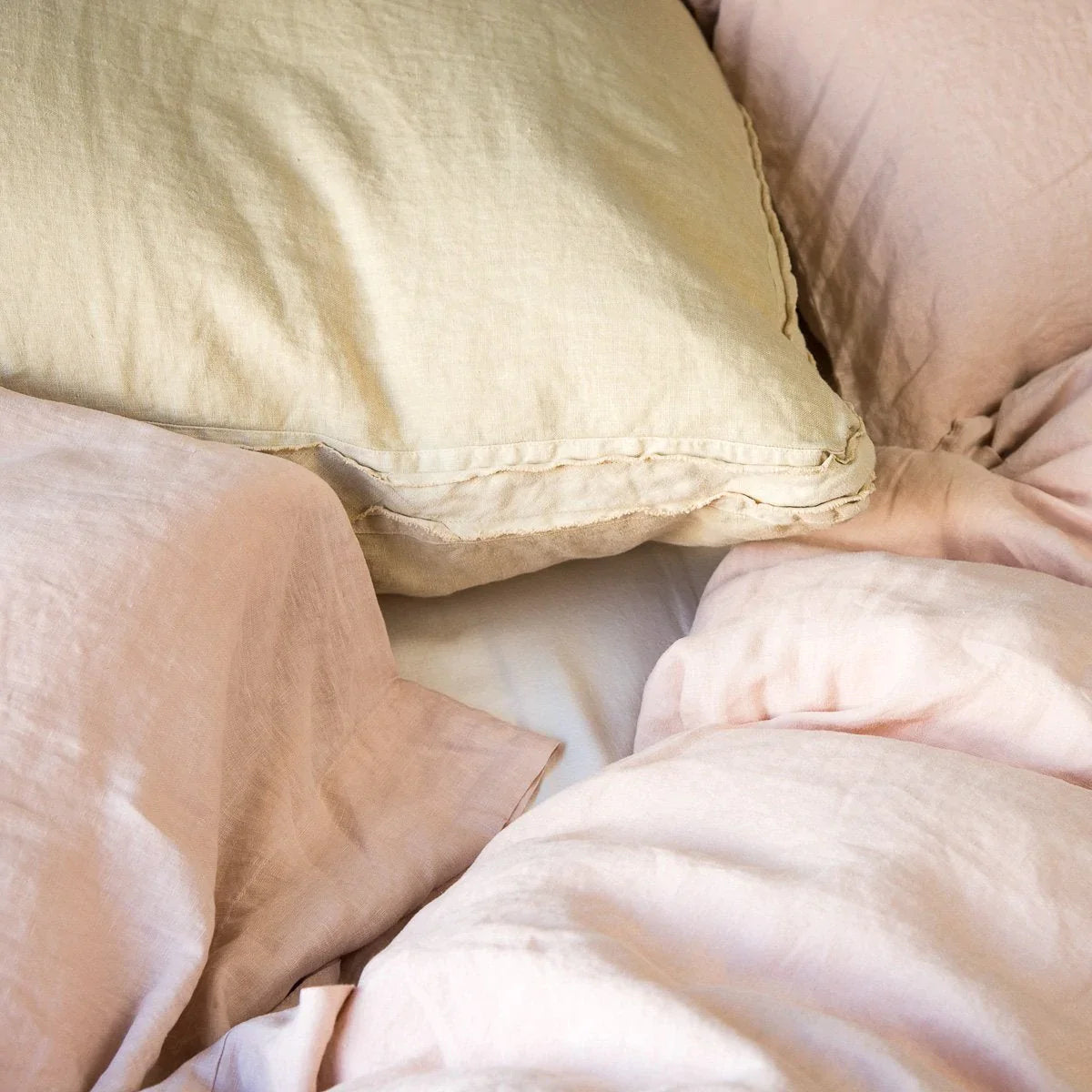 [allvariants]: Austin sham layered with pillows and duvet in pink and gold tones. Close up angle detailing raw edge trim.