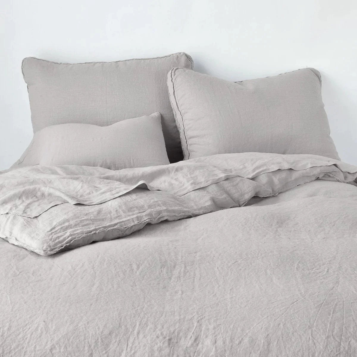 Fog: Midweight linen shams shown from foot of bed, leaning against a plain background with monochromatic bedding. 