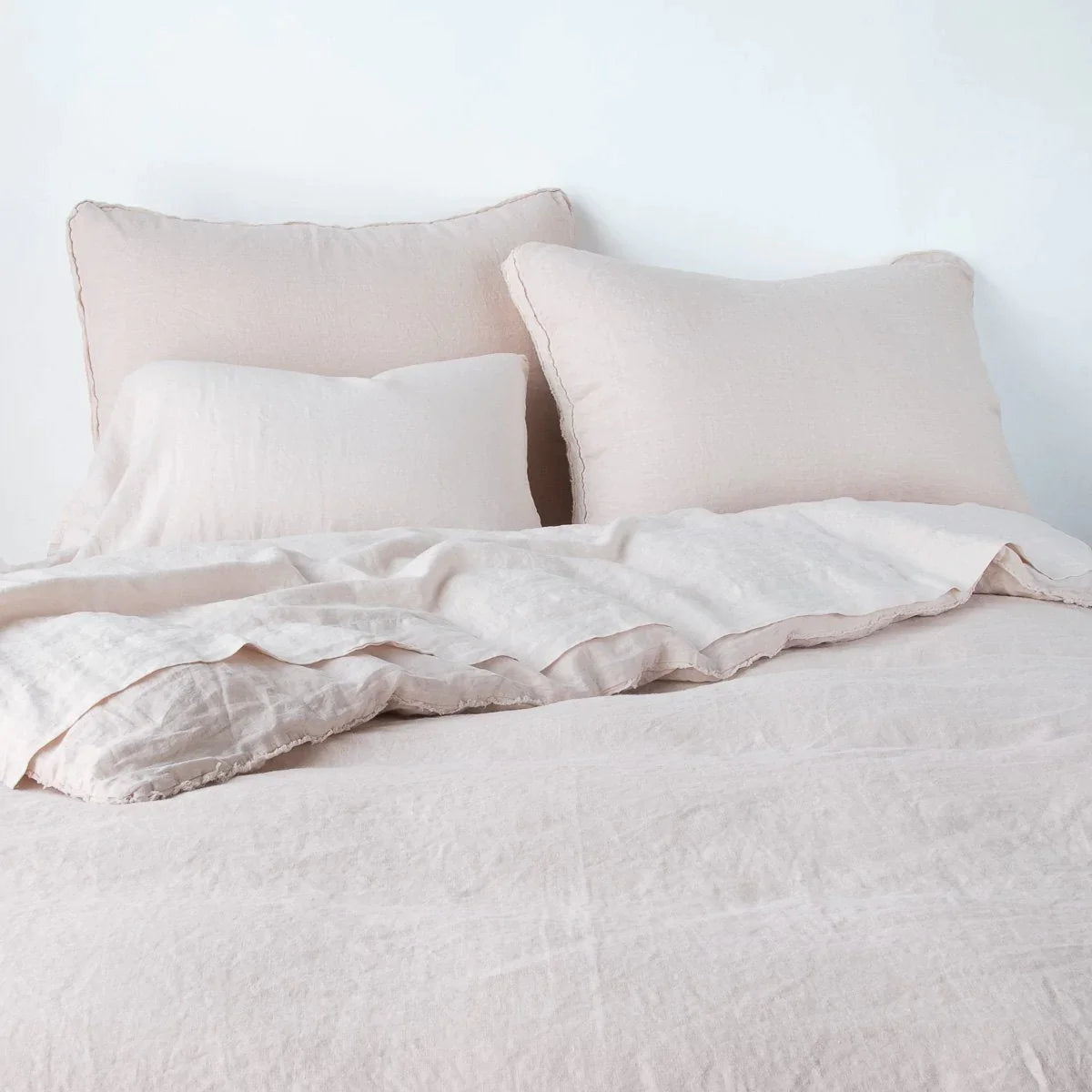 Pearl: Midweight linen shams shown from foot of bed, leaning against a plain background with monochromatic bedding. 