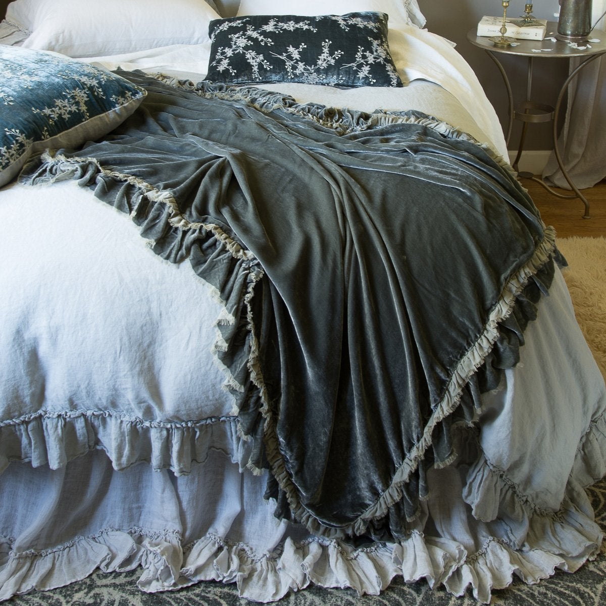 : Linen Whisper bed skirt in cloud, layered under a matching duvet cover and mineral silk velvet accessory pieces - end of bed view.