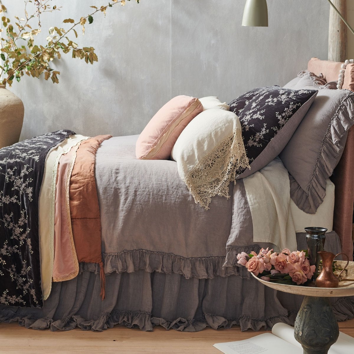 [allvariants]: Linen Whisper duvet cover in moonlight, shown with matching bed skirt and shams, and layered with accessory pieces in rouge and parchment - side view.