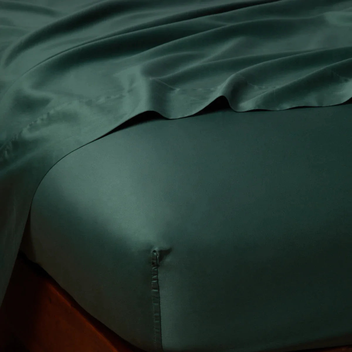 Jade: Cotton sateen flat sheet draped over matching fitted sheet. Shown from the top corner, the flat sheet is rumpled, highlighting the shine of the fabric.