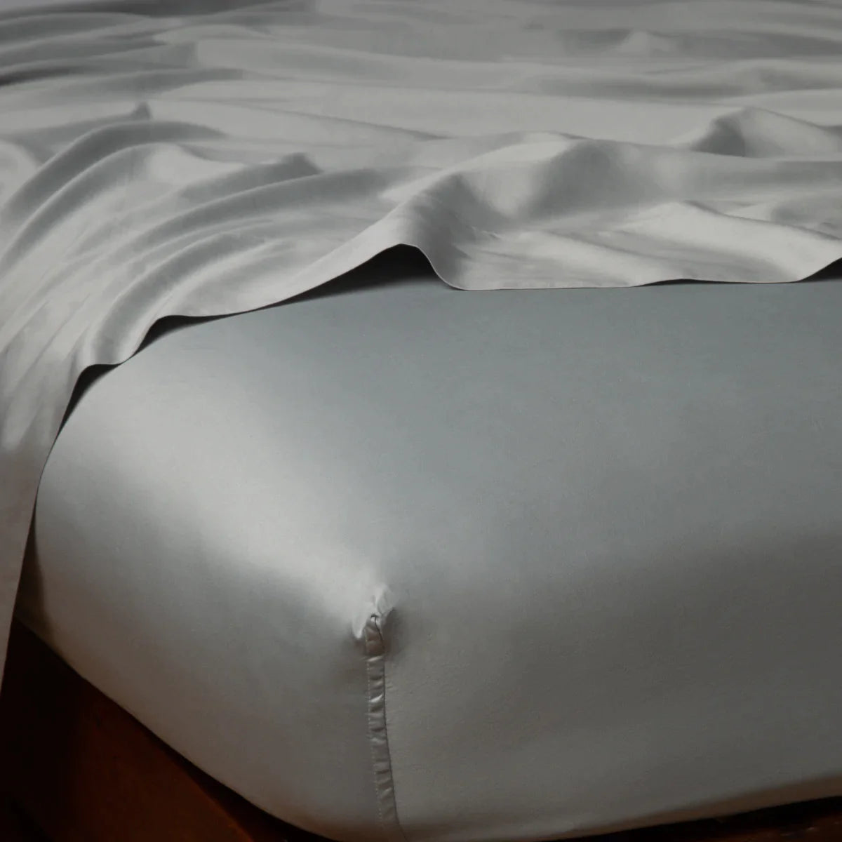 Mineral: Cotton sateen flat sheet draped over matching fitted sheet. Shown from the top corner, the flat sheet is rumpled, highlighting the shine of the fabric.