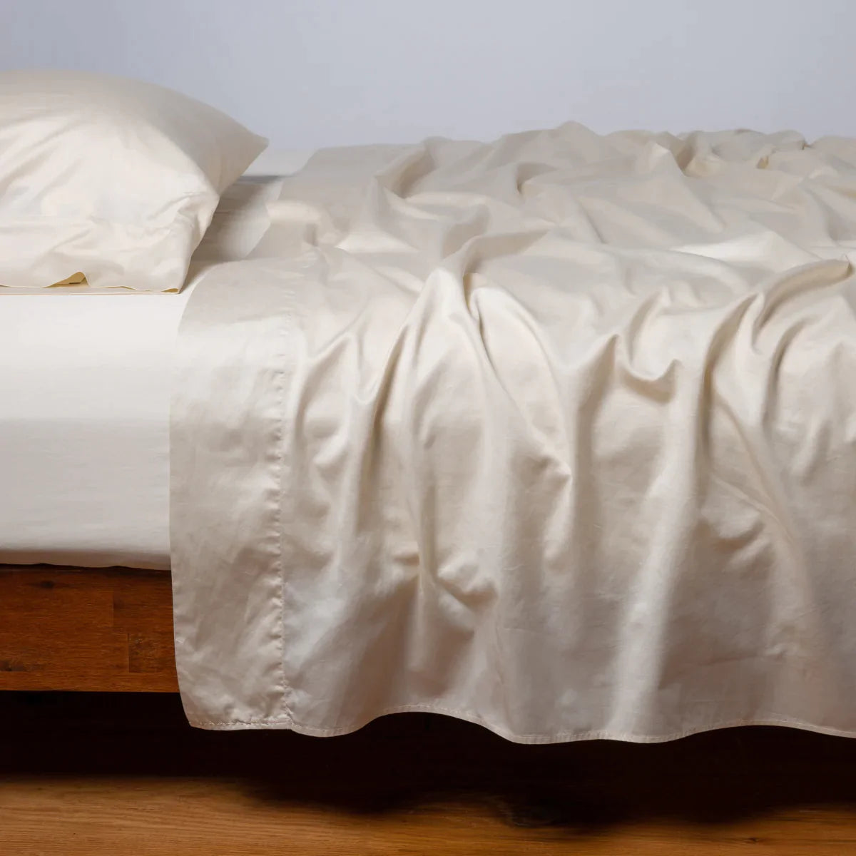 [allvariants]: Bria flat sheet in parchment, shown with matching fitted sheet and sleeping pillow - side view.